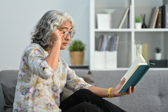 Elderly woman trying to read book having difficulties seeing text because of vision problems. - Stock Photo - Images