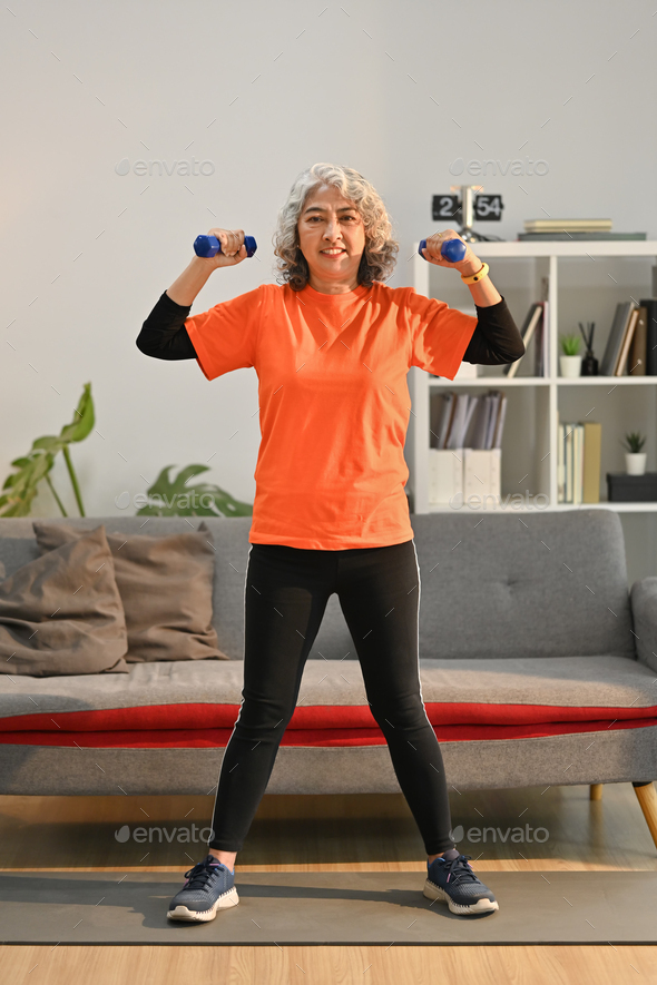 Full length shot of middle aged woman exercising with dumbbells at home. - Stock Photo - Images