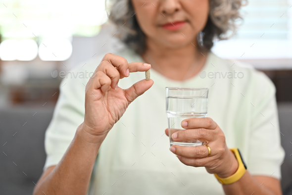 Middle aged woman holding pill and glass of water. Elderly healthcare concept. - Stock Photo - Images