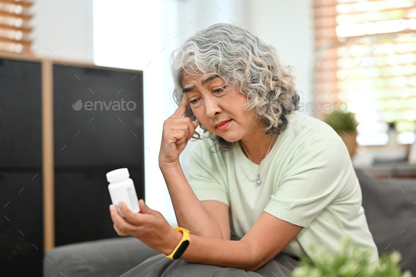 Worried middle aged woman taking medicine while sitting on couch at home.