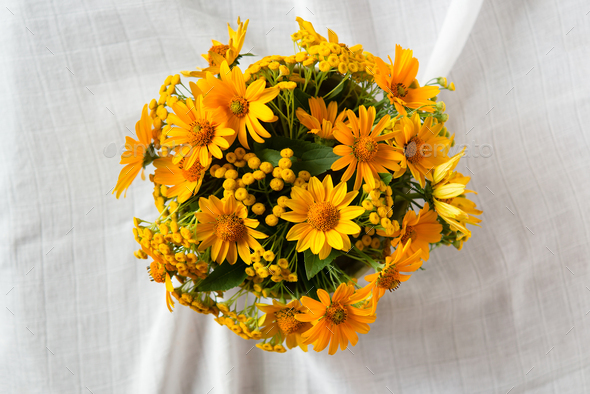 Bright yellow flowers in a round vase on a table with a white tablecloth