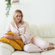 Smiling blonde woman sitting on comfortable coach in living room in pajama - homewear and free time - PhotoDune Item for Sale
