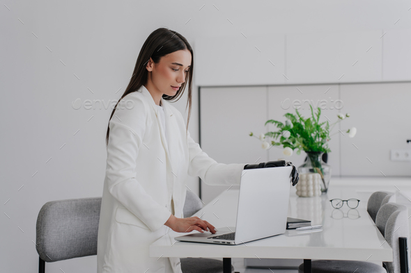 Purposeful young brunette woman in white suit opens laptop by bionic ...