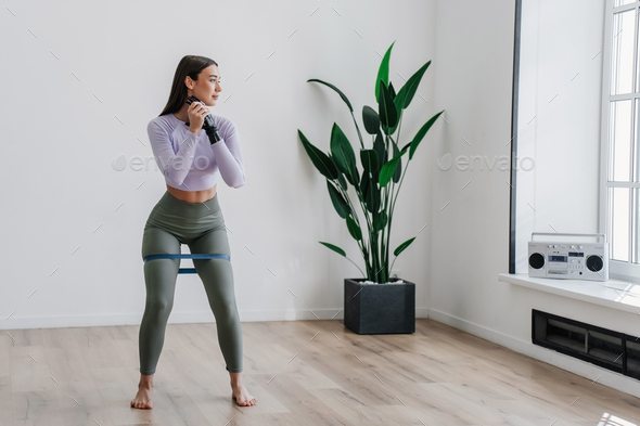 Pretty brunette fit girl in sportswear with artificial hand makes exercise at home uses rubber tapes