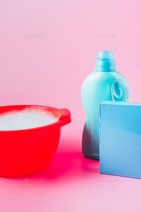 close up view of washing powder, laundry liquid and plastic basin with foam, pink background