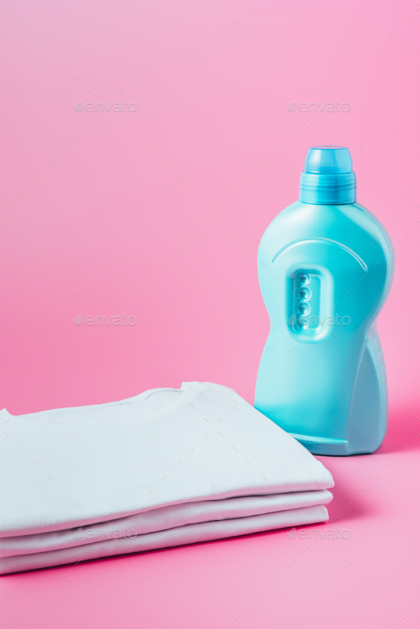 close up view of stack of white clean t-shirts and laundry liquid, pink background