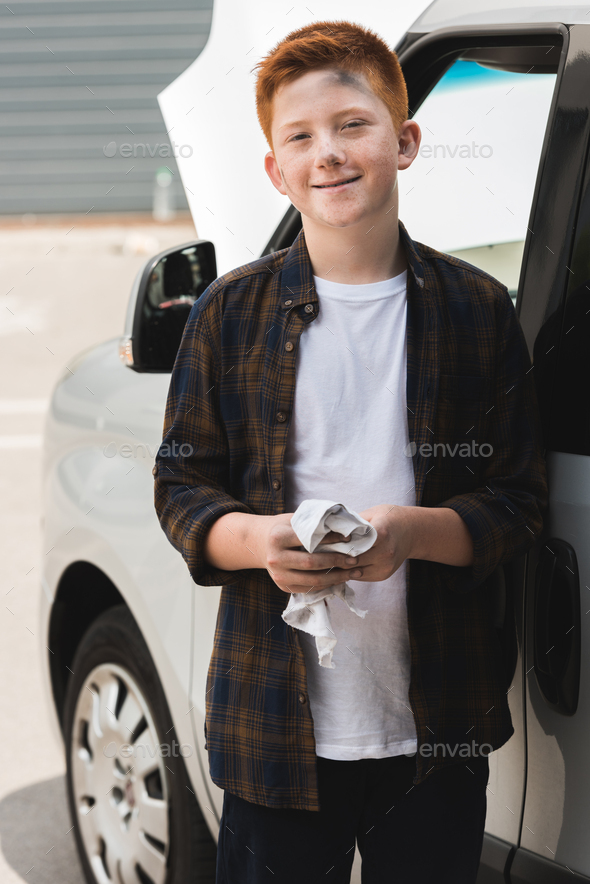 dirty red hair preteen boy cleaning hands after repairing car