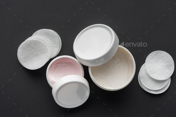 top view of bottles of cream and cosmetic pads isolated on black, beauty concept