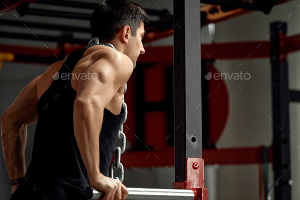 Weightlifter with a huge metal chain around his neck. Push-ups on the uneven bars in the gym