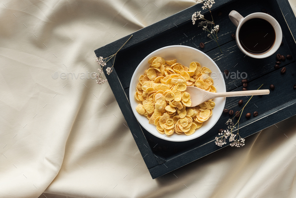 top view of bowl of cereal breakfast with cup of coffee on tray on beige cloth, breakfast in bed