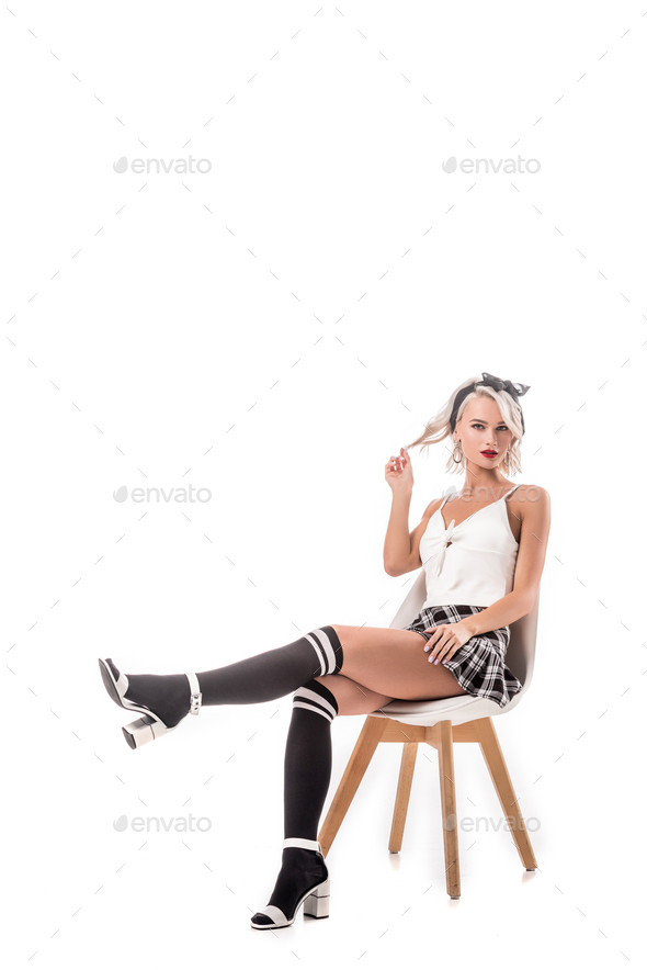 young blond woman in short plaid skirt and knee socks sitting on chair isolated on white