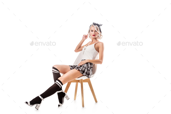 young blond woman in sexy short plaid skirt and knee socks sitting on chair isolated on white