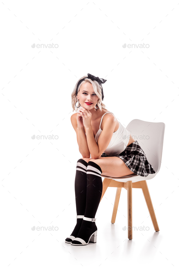 smiling blond woman in short plaid skirt and knee socks sitting on chair isolated on white