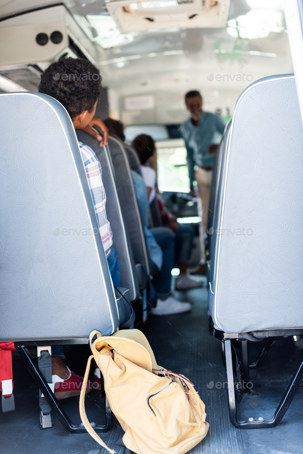 rear view of teen students sitting at school bus and listening to teacher