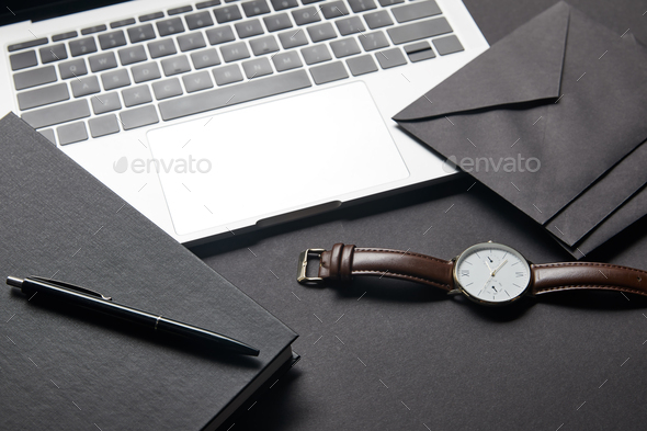 Laptop with black envelope and watch on black background
