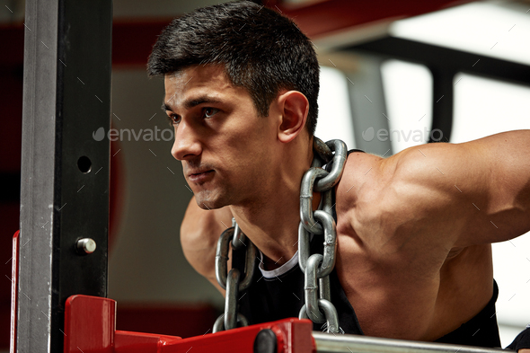 Weightlifter with a huge metal chain around his neck. Push-ups on the uneven bars in the gym