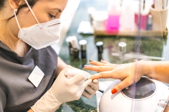 Shallow focus shot of a Hispanic female nail artist wearing a face mask painting a client's nails