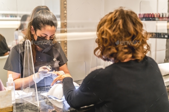 Shallow focus shot of a Hispanic female nail artist wearing a face mask painting a client's nails