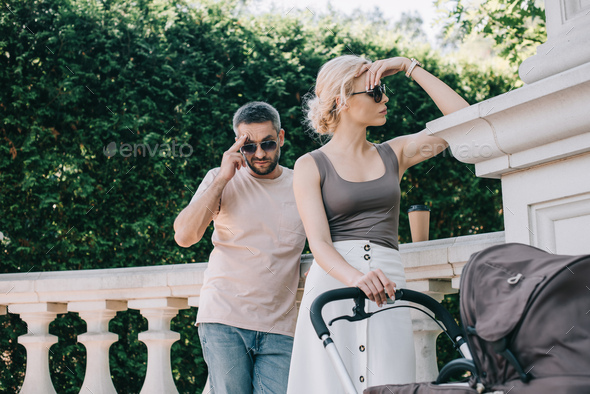 angry parents touching heads and looking away near baby carriage in park