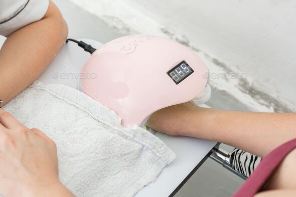 Woman getting a manicure for personal nail care with pink led nail lamp