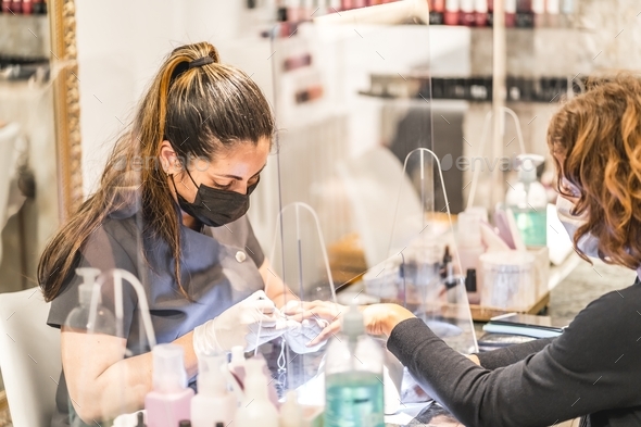 Shallow focus shot of a Hispanic female nail artist wearing a face mask painting a client\'s nails