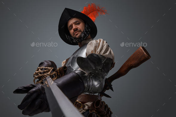 Portrait of antique musketeer pointing his sword to camera