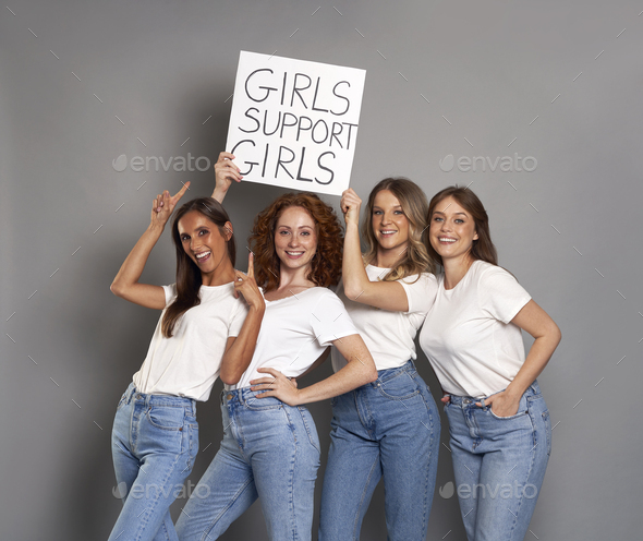 Four young caucasian women wearing blue jeans and white tshirt holding banner above head - Stock Photo - Images
