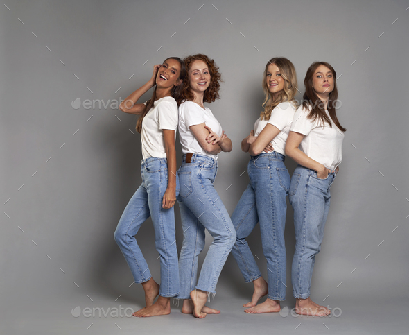Full length of four young caucasian women wearing blue jeans and white tshirt on grey background - Stock Photo - Images