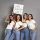 Four young caucasian women wearing blue jeans and white tshirt holding banner above head - PhotoDune Item for Sale