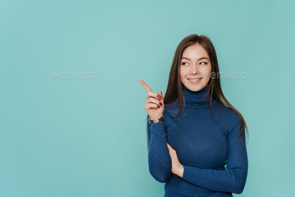 A beautiful European girl with long loose hair in blue sweater points by index finger to the side