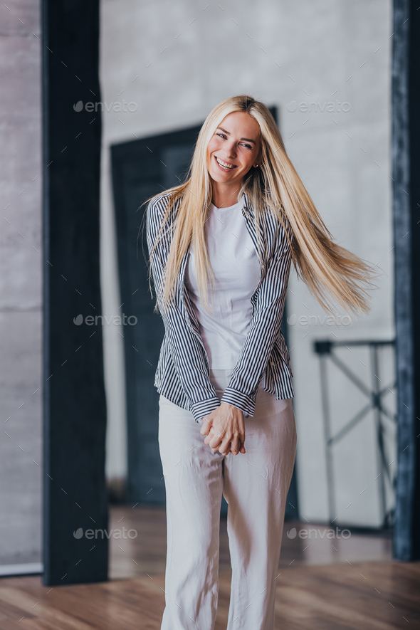 Vertical shoot of blonde Swedish girl in casual laughing comes in new apartment with fluttering hair - Stock Photo - Images
