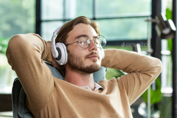 Close-up photo. A young freelancer, a programmer sits in the office wearing white headphones, hands - Stock Photo - Images