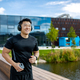 Smiling young Asian male athlete runner doing morning jog outside near lake wearing headphones and - PhotoDune Item for Sale