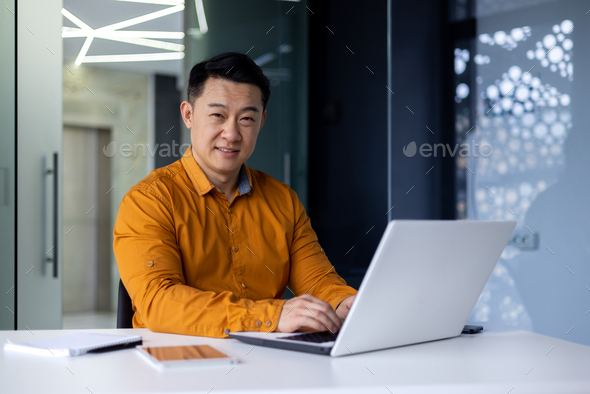 Portrait of happy and satisfied asian programmer inside office working with laptop, male freelancer - Stock Photo - Images