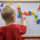 Back view of a blond toddler boy playing with colorful letters on a magnetic board - PhotoDune Item for Sale