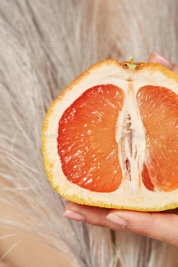 close-up half of a juicy grapefruit in a female hand, symbolizing the female genital organs