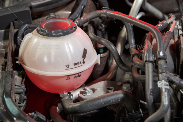 car plastic expansion tank with red antifreeze labeled max and min. Underhood with black tubes