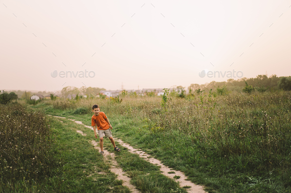 Portrait of a smiling little boy in a orange T-shirt and playing outdoors on the field at sunset - Stock Photo - Images