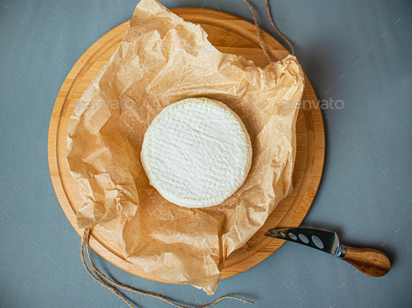 camembert cheese, round brie on kraft paper, cheese, on a cutting board, and a knife