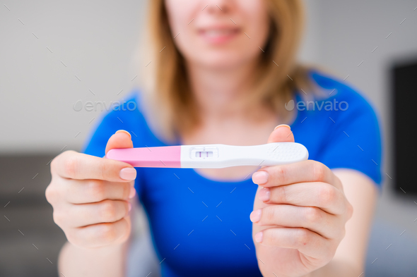 Blonde smiling woman holding a positive pregnancy test