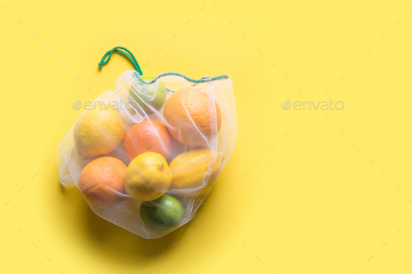 Fruits in reusable eco-friendly mesh bags on yellow. Zero waste. Ecological concept. Stop pollution.