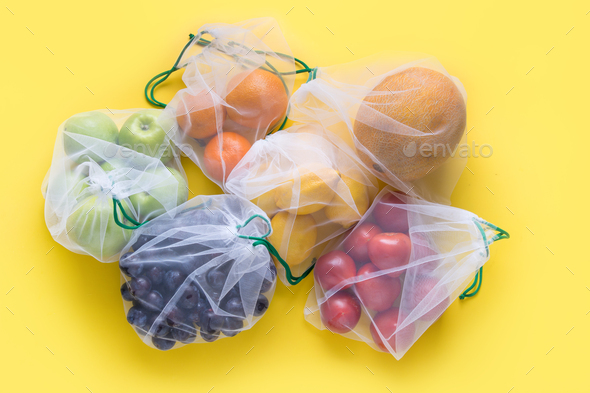 Fruits in reusable eco-friendly mesh bags on yellow. Zero waste. Ecological concept. Stop pollution.