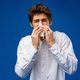 A young man sneezes into a napkin over blue background - PhotoDune Item for Sale