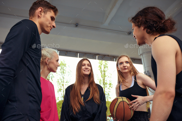 A friendly company of guys and girls are having fun on the basketball court, they are going to play
