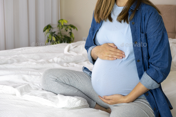 Pregnant woman in blue t-shirt and jeans shirt sitting in bed.