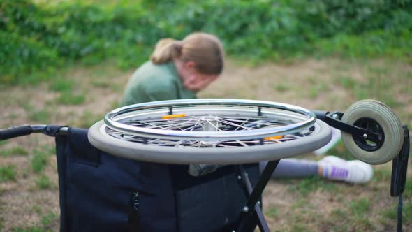 Wheel of Rolled Over Wheelchair Spinning with Blurred Disabled Girl Crying at Background alt