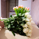 Woman put white roses flowers bouquet on wooden table against tulips. - PhotoDune Item for Sale