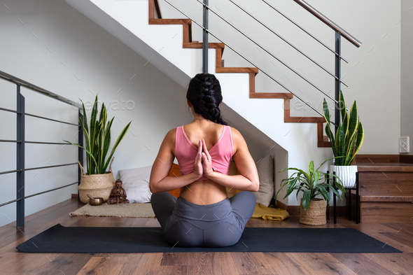 Rear view of woman doing reverse prayer yoga pose at home living room. Female doing namaste mudra.