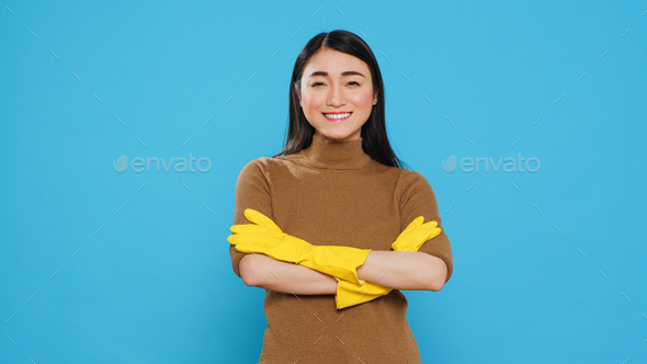 Smiling professional maid wearing protective rubber gloves standing with arm crossed in studio
