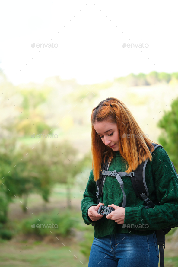 Hiker redhead young woman fastening backpack strap in the mountain.